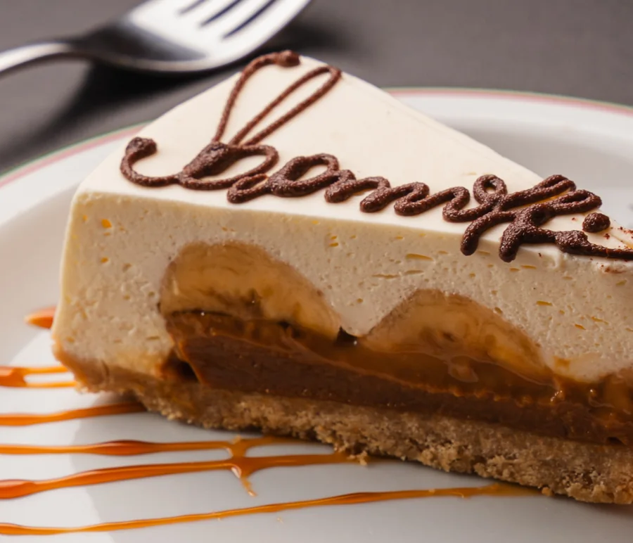 Fatia de Banoffi vista de lado: bolacha, doce de leite, banana, nata e a assinatura em chocolate